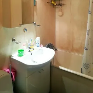 На фото: часть помещения санузла, керамическая раковина со смесителем на тумбе, на раковиной - навесной шкафчик с зеркалом, справа - ванная со смесителем