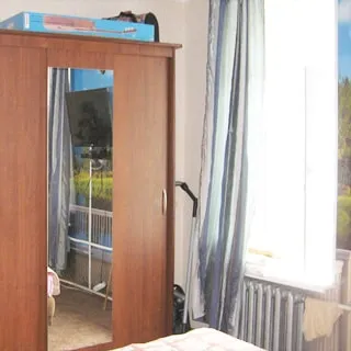 На фото: часть помещения жилой комнаты, окно, под окном - радиатор центрального отопления, слева от окна - платяной шкаф-купе, стены оклеены обоями