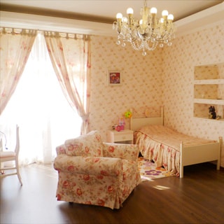 На фото: часть комнаты, одно окно, кровать у стены справа от окна, у кровати тумбочка, мягкое кресло, полы - ламинат, на потолке - люстра.