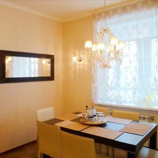 На фото: часть комнаты, окно, обеденный стол со стульями у окна, на стене - зеркало, полы - плитка, на потолке - люстра.