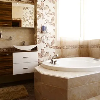 На фото: часть помещения санузла с ванной, окно, перед окном - ванная со смесителем, слева - раковина со смесителем на тумбе, навесной шкафчик с зеркалом, полы и стены - плитка.