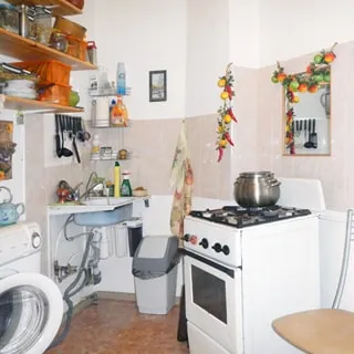 На фото: часть помещения кухни, 4-комфорочная газовая плита с духовкой, раковина, стиральная машина, навесные кухонные полки, полы - линолеум, стены облицованы плиткой