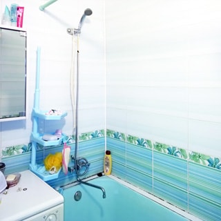На фото: ванная комната, смеситель, стиральная машина, ванная голубого цвета, стены облицованы плиткой.
