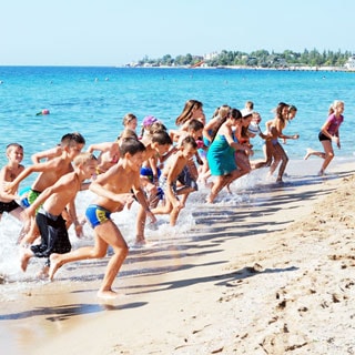 На фото: море, песчаный пляж, выбегающие из моря после купания дети