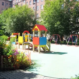 На фото: часть светлого благоустроенного зеленого двора с детской площадкой и цветочными клумбами.