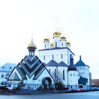 На фото: православный собор с золотыми куполами на огороженном участке, прилегающая территория - улица с припаркованными автомобилями, на дальнем плане справа - кирпичная стена, похожая на кремлевскую.