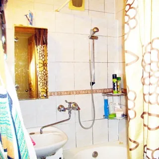 На фото: часть ванной, керамическая раковина, над раковиной - зеркало, справа - ванна, смеситель общий для раковины и ванны, стены - плитка.
