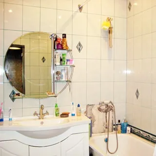 На фото: ванная комната, широкая керамическая раковина со смесителем, зеркало с полкой, ванная со смесителем, стены облицованы светлой керамической плиткой