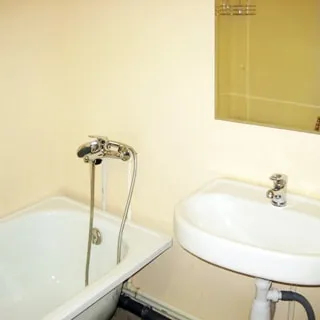 На фото: часть санузла, ванная со смесителем, керамическая раковина со смесителем, над раковиной - зеркало, стены окрашены