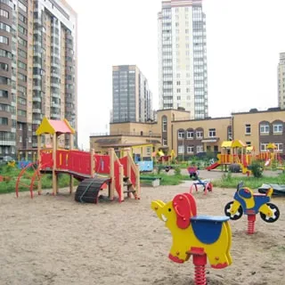 На фото: часть дворовой территории, большая оборудованная детская площадка, примыкающая к детскому саду, вокруг детской площадки - газон
