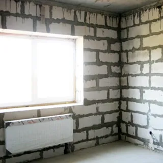 На фото: часть комнаты с окном, установлен стеклопакет, под окном - радиатор отопления, стены - пеноблоки без отделки, пол - цементно-песчаная стяжка