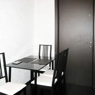 На фото: чистая комната со свежим ремонтом, качественная входная дверь, светлые обои, полы - темный ламинат, слева от двери у стены - стол, у стола - четыре мягких стула.