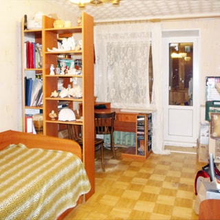 На фото: чистая комната, светлая мебель, светлые обои, полы - светлый паркет, окно - стеклопакет и балконная дверь, у окна - письменный стол, слева у стены - диван и книжный шкаф