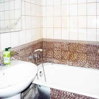На фото: часть ванной комнаты, ванная со смесителем для ванной, керамическая раковина со смесителем, над раковиной - зеркало, стены - плитка в бежевых тонах