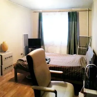 На фото: часть помещения жилой комнаты, одно окно, под окном - батарея центрального отопления, слева от окна в углу - тумба с телевизором, справа у стены - разложенный диван-кровать, перед ним на переднем плане - кресло