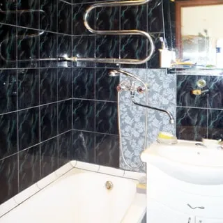 На фото: часть помещения ванной, слева у стены - эмалированная ванная, справа от нее - керамическая мойка на тумбе с дверцами, общий смеситель для манной и мойки, над мойкой - полка и зеркало, стены облицованы керамической плиткой