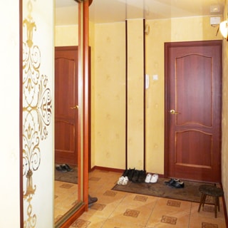 На фото: часть помещения прихожей, прямо входная дверь, слева от двери на стене - домофон, у левой стены - шкаф-купе с зеркальной дверью, стены оклеены обоями, полы - плитка, перед дверью коврик для обуви, справа у стены - табурет