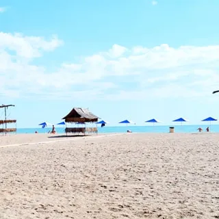 На фото: часть территории песчаного пляжа, зонтики от солнца, душевые кабинки, песок, море и голубое небо с легкими облачками