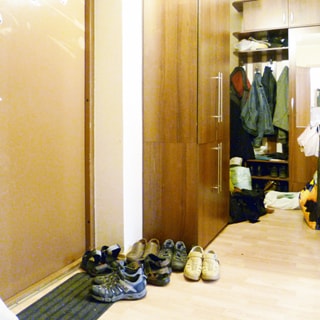 На фото: часть помещения прихожей, слева входная металлическая дверь, справа от входной двери - одежный шкаф, за ним еще один шкаф с открытой секцией для верхней одежды, полы - линолеум