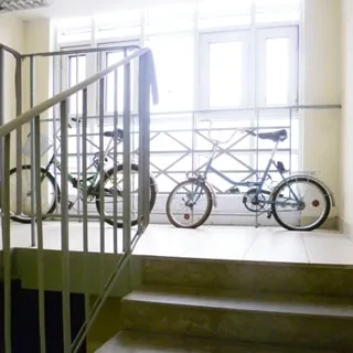 На фото: часть лестничной клетки, сплошное остекление, очень светло, ступени и площадка облицованы керамической плиткой, перила лестницы - металлические, у наружного окна - металлическое защитное ограждение, у окна - два велосипеда