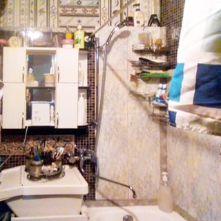 На фото: часть помещения ванной комнаты, справа у стены - ванная, слева от нее - керамическая раковина с общим смесителем для раковины и ванны, над раковиной на стене - навесной туалетный шкафчик с полочками и зеркалом, стены облицованы керамической плиткой