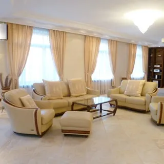 На фото: часть помещения жилой комнаты - гостиной, три окна, мягкая мебель: два дивана и два кресла, журнальный столик со стеклянной столешницей, на потолке - люстра, полы - плитка