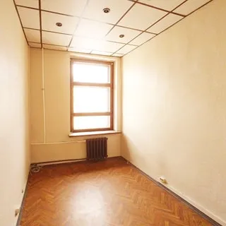 На фото: часть помещения комнаты без мебели, одно окно, под окном - радиатор центрального отопления, полы - линолеум, потолки - подвесные, установлены точечные светильники