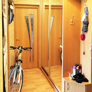 На фото: часть помещения прихожей, справа у стены - одежный шкаф-купе, правее - вешалка для одежды и тумбочка для обуви, слева у стены - велосипед, прямо - дверь в комнату, полы - ламинат