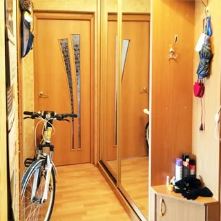 На фото: часть помещения прихожей, справа у стены - одежный шкаф-купе, правее - вешалка для одежды и тумбочка для обуви, слева у стены - велосипед, прямо - дверь в комнату, полы - ламинат