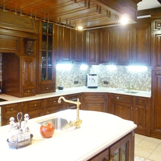 На фото: часть помещения кухни, встроенная кухонная мебель вдоль стены, остров с мойкой и столешницей, фасады - дерево, фартук - плитка, местное освещение, на столешнице в углу - кофеварка, полы - плитка