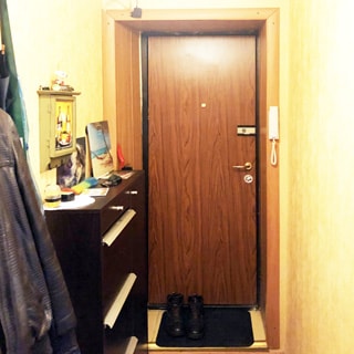 На фото: часть помещения прихожей, металлическая входная дверь, справа от двери - домофон, слева от двери у стены - комод для обуви и настенная вешалка для верхней одежды, стены оклеены обоями