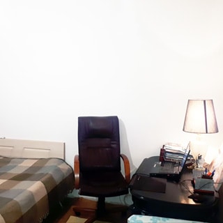 На фото: часть жилой комнаты, слева - диван-кровать застелена пледом, справа от нее - офисное кресло, правее - журнальный столик с настольной лампой и ноутбуком, стены - окрашены
