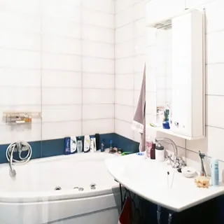 На фото: часть помещения ванной комнаты, прямо у стены в углу - ванна с гидромассажем и гибким душем со смесителем, справа от ванны - керамическая раковина со смесителем, над раковиной на стене навесной шкафчик с зеркалом и подсветкой, стены облицованы керамической плиткой