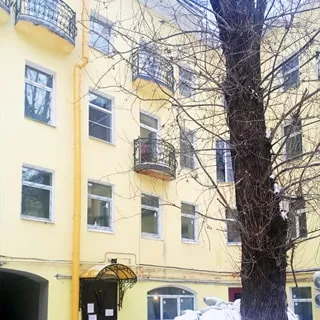 На зимнем фото: часть фасада жилого дома, парадная под козырьком, окна - стеклопакеты, в некоторых квартирах - небольшие балконы, слева от парадной - арка, в цокольном этаже - витринное окно нежилого помещения