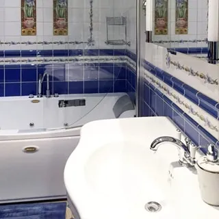 На фото: часть помещения ванной, совмещенной с санузлом. Прямо у стены - ванна с гидромассажем, справа на стене - широкая керамическая раковина со смесителем, над ней на стене - зеркало с подсветкой, стены и пол - керамическая плитка с рисунком