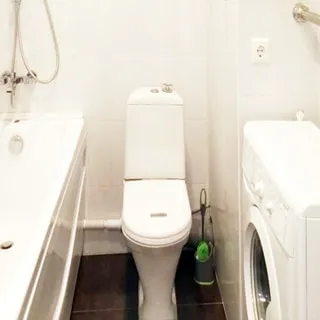 На фото: часть помещения совмещенного санузла, слева у стены - ванная со смесителем, справа от нее - унитаз-компакт, правее - стиральная машина с фронтальной загрузкой, над ней на стене - полотенцесушитель, стены и полы - керамическая плитка