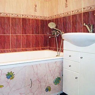 На фото: часть помещения ванной комнаты, прямо у стены - ванная со смесителем, справа от ванны - керамическая мойка на тумбе-шкафу со своим смесителем, стены облицованы керамической плиткой
