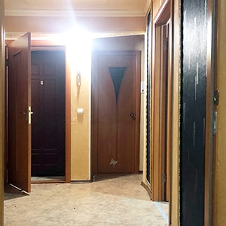 На фото: часть помещения прихожей, слева впереди - входная двойная дверь (наружная - металлическая, внутренняя - деревянная), справа от входной двери - светильник на стене и входная дверь в санузел, справа дверь в комнату, стены оклеены обоями, полы - линолеум