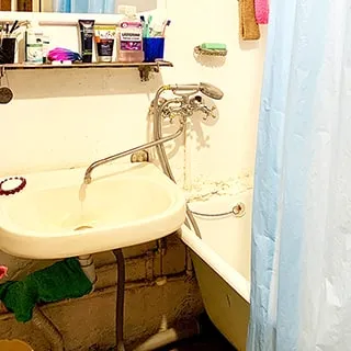 На фото: часть помещения ванной комнаты, справа - ванна, частично укрытая занавеской, слева от ванны на стене - керамическая раковина, смеситель общий на раковину и ванну, над раковиной - полочка с туалетными принадлежностями, над ней - зеркало, стены окрашены