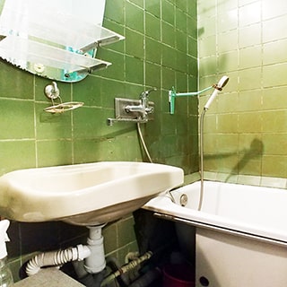 На фото: часть помещения ванной комнаты, у дальней стены установлена ванна, на левой стене - керамическая раковина на кронштейнах, смеситель общий на ванну и раковину, над раковиной на стене - полочка для туалетных принадлежностей и зеркало, стены облицованы керамической плиткой