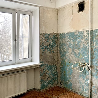 На фото: часть помещения кухни без мебели, без плиты и без мойки, одно окно, установлен стеклопакет, за окном видна стена соседнего дома и деревья на улице, под окном - радиатор центрального отопления, потолок окрашен, стены подготовлены под выравнивание, пол - линолеум