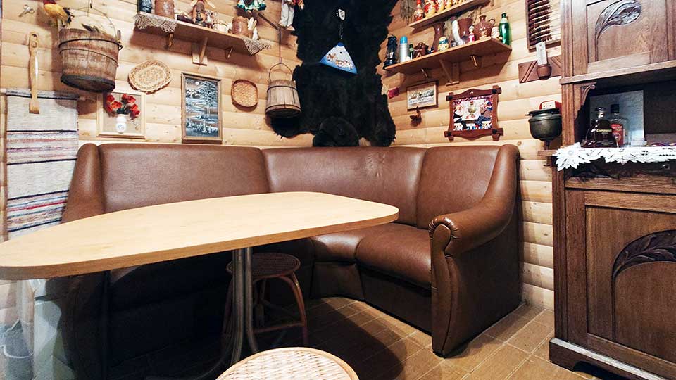 На фото: небольшое помещение для отдыха после сауны, полы - плитка, стены обшиты блок-хаусом, справа у стены - высокий комод, прямо в углу - угловой мягкий диван, перед ним небольшой стол, на стенах полки, на полках посуда и декоративные украшения