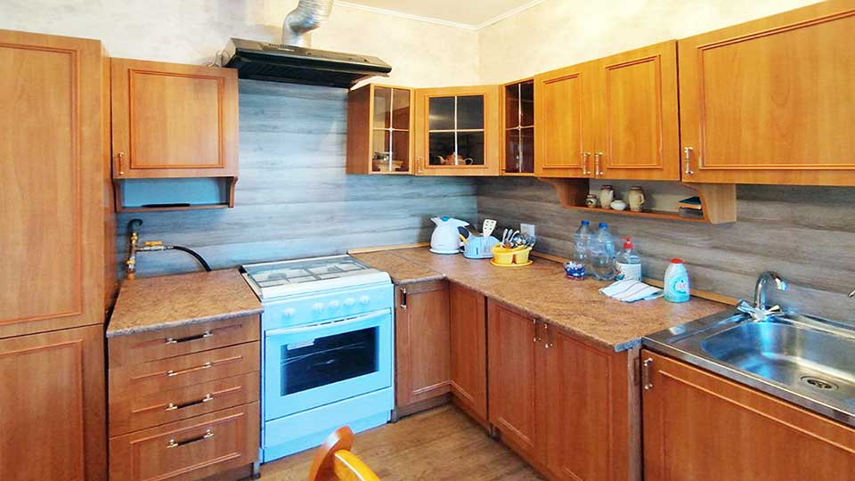 На фото: угловая кухня из тумб с общей столешницей и навесных шкафов, газовая двухкомфорочная плита с духовым шкафом, над плитой - вытяжка, мойка со смесителем расположена в правой части кухни