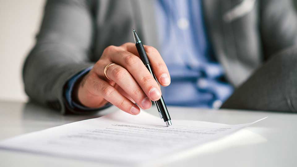 На фото: мужчина с ручкой в руке за столом перед подписанием договора.